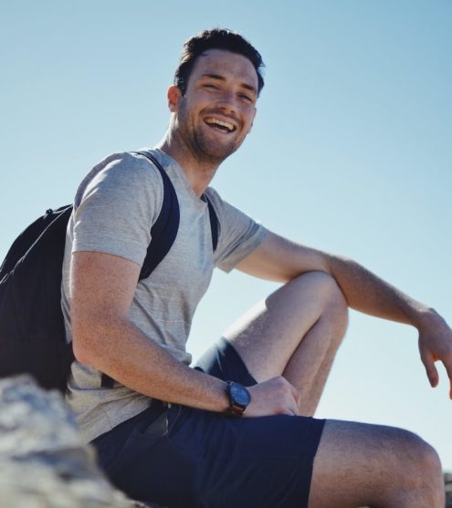 smiling man sitting on gray rock at daytime